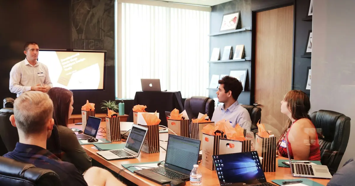 Man standing in front of people sitting beside table with laptop computers